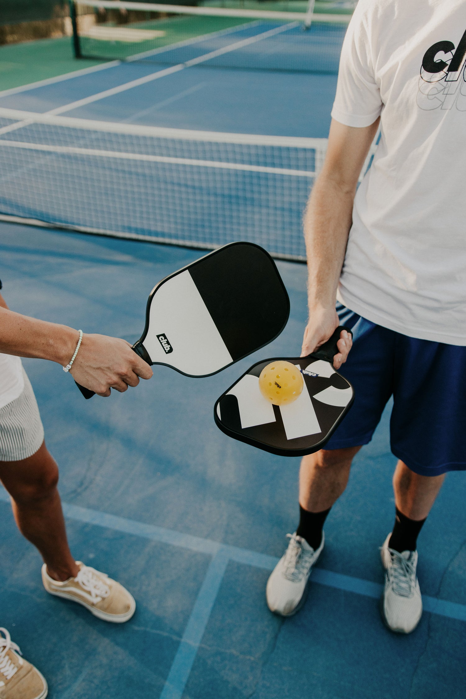 two people hold black and white pickleball paddles